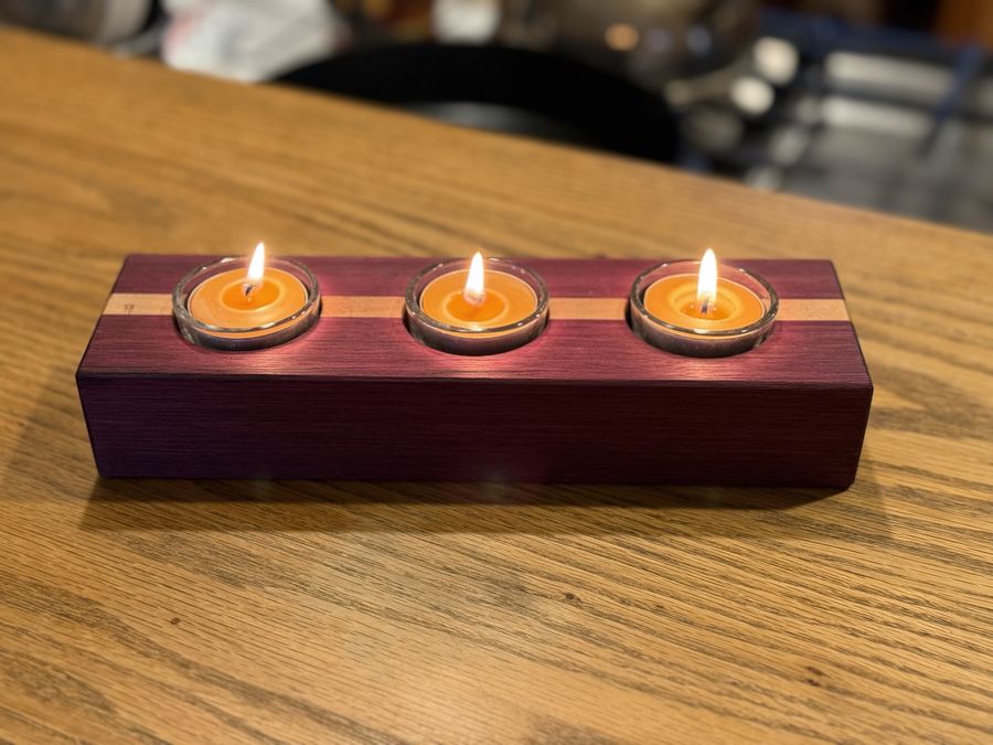 A purpleheart tealight holder with a pale stripe, three candles lit.