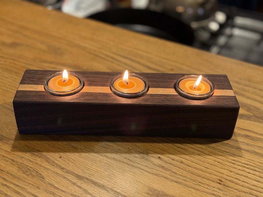 A walnut tealight holder with a pale stripe, three candles lit.