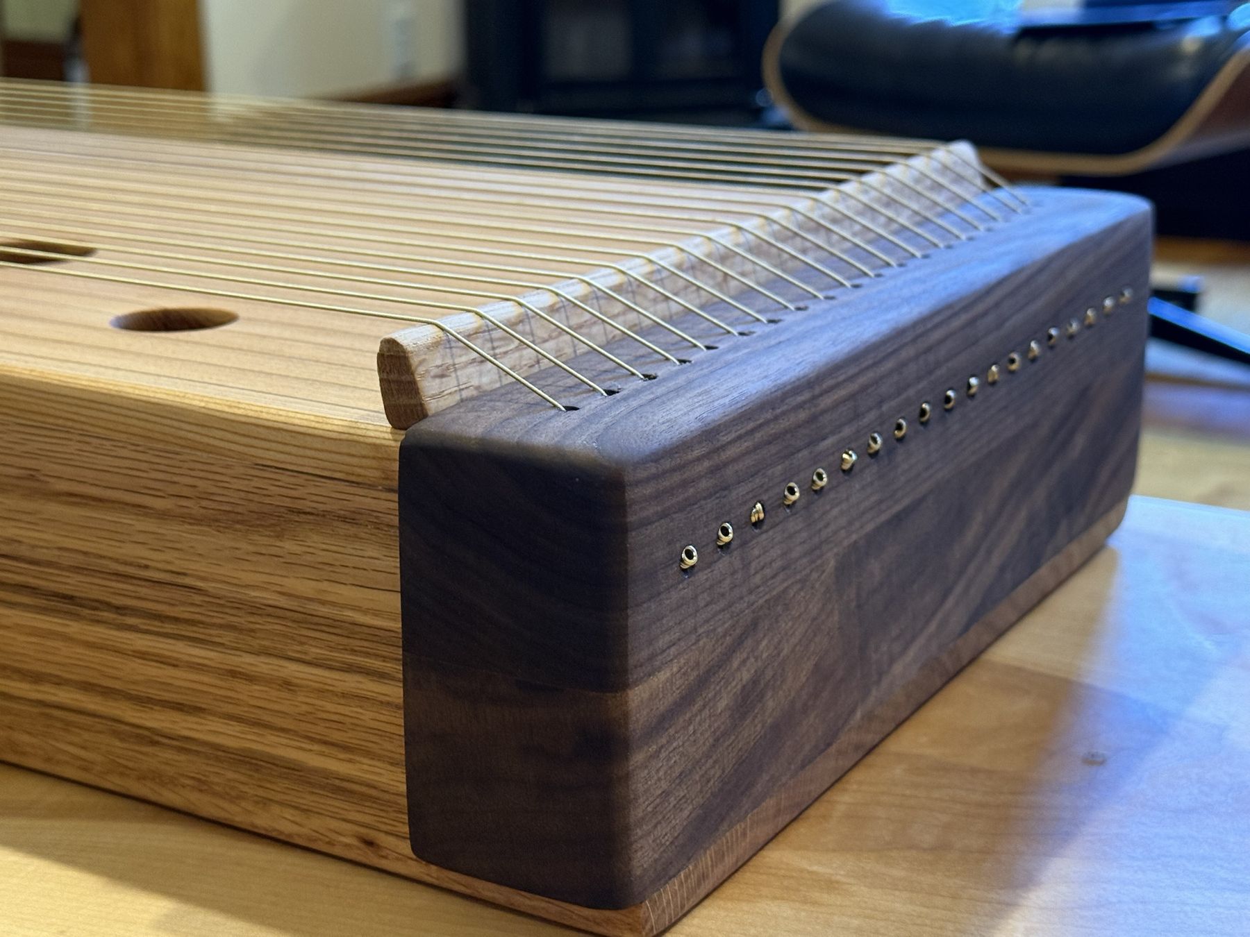 The far end of the monochord: strings pass over an oak bridge and through a row of brass eyelets in a rounded walnut block.